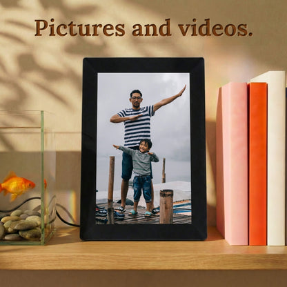 A vertically standing 10-inch black Family Frame digital memory display resting on a warm wooden shelf next to colorful books. Equipped with advanced processing, this premium digital picture frame flawlessly handles both high-definition photo and video playback to capture full, dynamic memories. The robust photo sharing frame allows distant relatives to securely send video messages directly to any living space.
