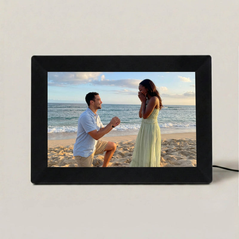 A 10-inch black Family Frame digital picture frame resting on a minimalist beige surface, showcasing a vibrant edge-to-edge photograph. This sleek smart picture frame features an HD digital photo display designed to keep cherished memories central to everyday life. Functioning as the ultimate long-distance family gift, this WiFi photo frame seamlessly connects separated loved ones with absolutely zero subscription fees.
