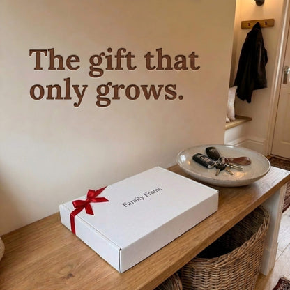 A 10-inch black Family Frame smart picture frame packaged elegantly in a white gift box with a red bow, sitting on a wooden entryway bench. Perfectly presented as a luxury long-distance family gift, this beautifully boxed WiFi photo frame is built to foster daily emotional connections. The premium electronic photo frame serves as a continuous digital memory display, updating effortlessly through its dedicated secure application.
