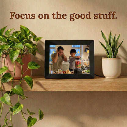 A 10-inch black Family Frame smart picture frame situated on a light wooden shelf alongside vibrant green houseplants. Delivering an unparalleled high-resolution display, this electronic photo frame beautifully highlights the vivid details of every uploaded image. Acting as a dedicated digital memory display, it bridges physical distance between family members with a constant stream of new photos.
