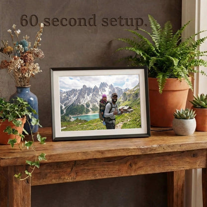A 10-inch classic black Family Frame electronic photo frame framed by a white mat, displayed prominently on a rustic entryway table surrounded by plants. Prioritizing accessibility, this intuitive smart picture frame boasts a frictionless, easy 60-second WiFi setup process that anyone can master. This no subscription fee digital frame ensures immediate and uninterrupted photo sharing for families of all technical backgrounds.
