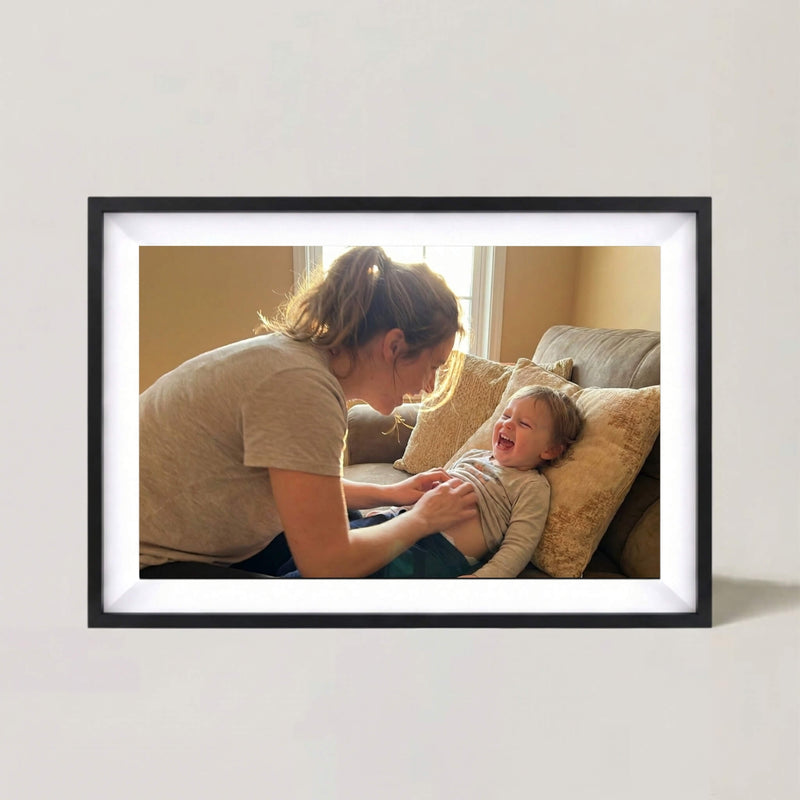 A 10-inch cordless classic black Family Frame digital picture frame with a white mat resting on a neutral surface, illuminating a shared family portrait. This premium battery-powered smart picture frame features an HD digital photo display that can be placed anywhere without being tethered to a wall outlet. Built as the ultimate long-distance family gift, this wire-free WiFi photo frame seamlessly connects loved ones across the country with zero subscription fees.
