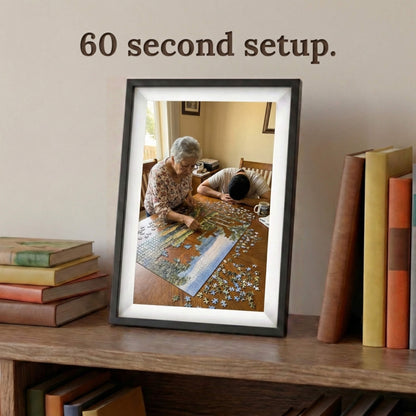 A 10-inch cordless classic black Family Frame electronic photo frame framed by a white mat, displayed prominently on a bookshelf beside stacked books. Prioritizing accessibility, this intuitive battery-powered smart picture frame boasts a frictionless, easy 60-second WiFi setup process that anyone can master. This no subscription fee digital frame ensures immediate and uninterrupted photo sharing for families of all technical backgrounds.
