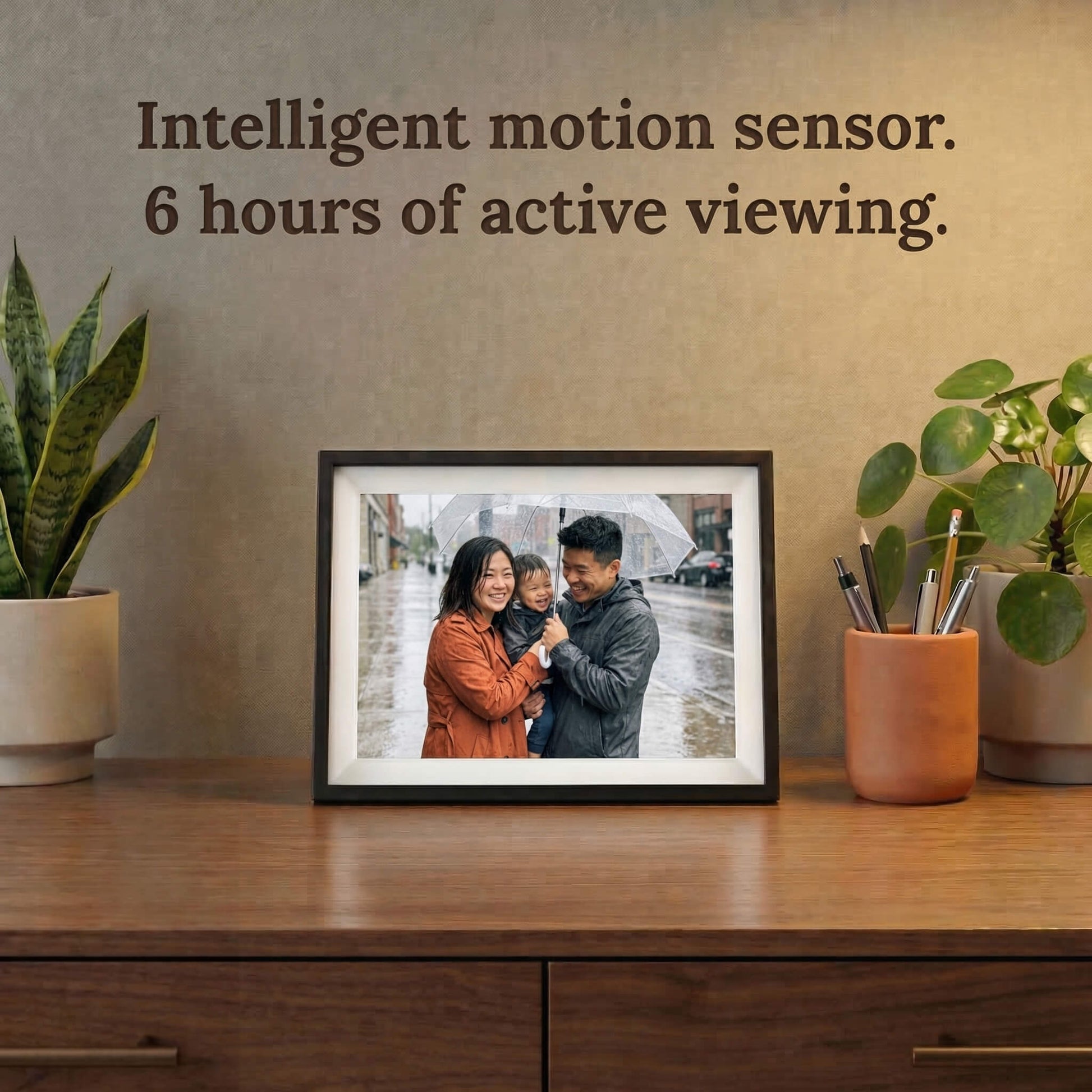 A 10-inch cordless classic black Family Frame smart picture frame with a classic white mat resting on a dark wood credenza surrounded by houseplants. Highlighting its completely cordless design, this electronic photo frame features an intelligent motion sensor and rechargeable battery for up to 6 hours of active, wire-free viewing. This innovative WiFi photo frame is the perfect long-distance family gift, allowing memories to be displayed on any surface without worrying about nearby outlets.
