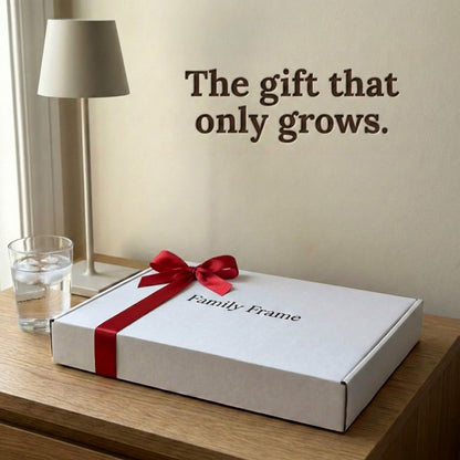 A 10-inch cordless classic black Family Frame smart picture frame packaged elegantly in a white gift box with a red bow, sitting on a bedside table beside a reading lamp. Perfectly presented as a luxury long-distance family gift, this beautifully boxed cordless WiFi photo frame is built to foster daily emotional connections. The premium electronic photo frame serves as a continuous digital memory display, updating effortlessly through its dedicated secure application.
