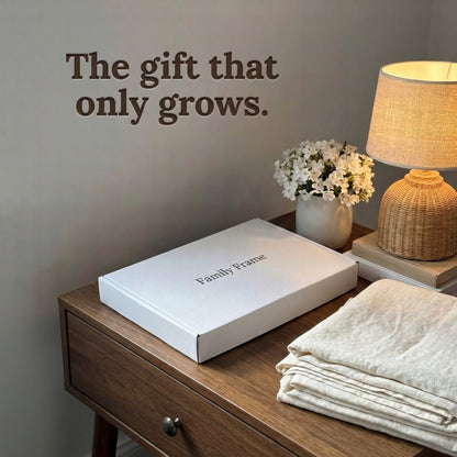 A 10-inch cordless mocha wood Family Frame smart picture frame packaged elegantly in a clean white gift box, sitting on a bedside nightstand next to folded linens. Perfectly presented as a luxury long-distance family gift, this beautifully boxed cordless WiFi photo frame is built to foster daily emotional connections. The premium electronic photo frame serves as a continuous digital memory display, updating effortlessly through its dedicated secure application.
