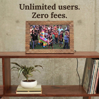 A 10-inch oak wood Family Frame digital picture frame placed on an open wooden shelving unit beside modern home accents. Built to gather the whole family, this smart picture frame securely accepts instant photo uploads from an unlimited number of invited users around the globe. Operating entirely as a no subscription fee digital frame, it represents the most cost-effective way to maintain long-distance family connections over time.
