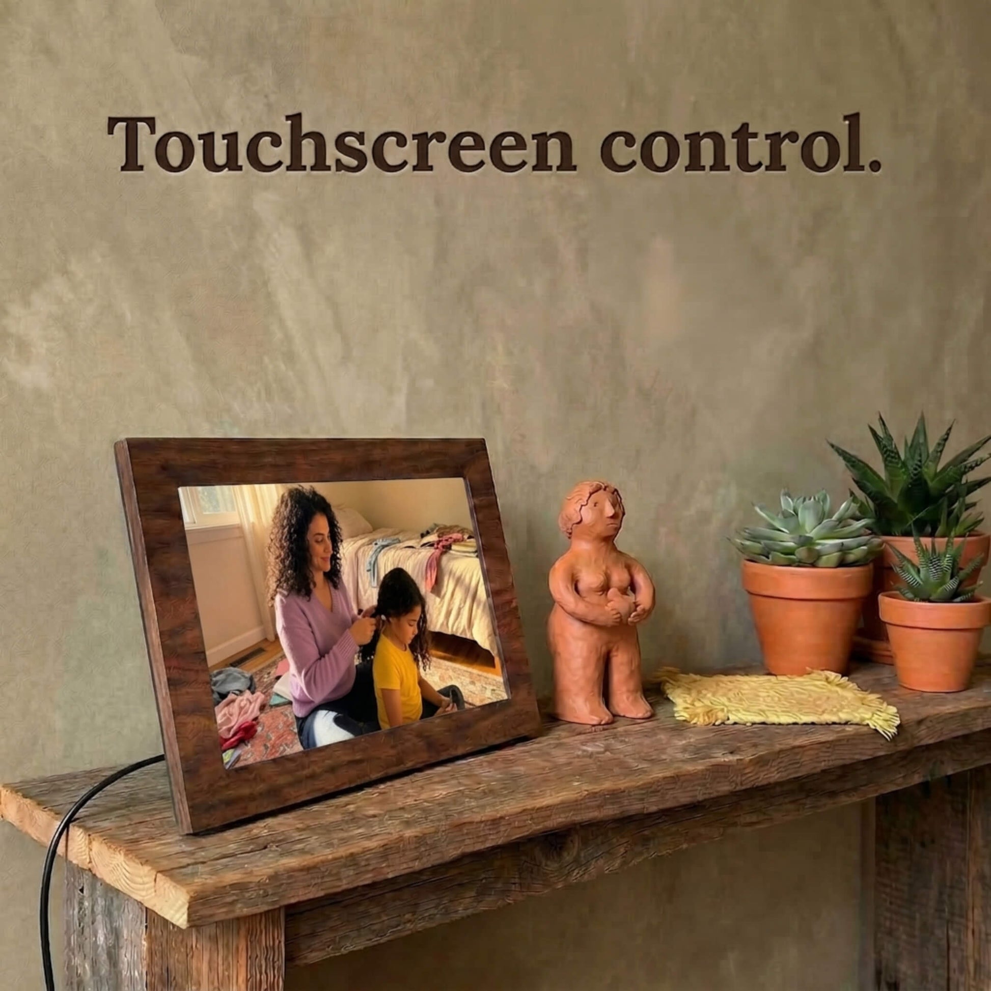 A 10-inch oak wood Family Frame photo sharing frame resting on a weathered rustic table surrounded by small succulent plants. This high-end WiFi photo frame provides an effortless user experience through a highly responsive, intuitive touchscreen control interface. Recognized as an ideal long-distance family gift, it offers unlimited users the ability to curate daily photo updates completely free of subscription charges.