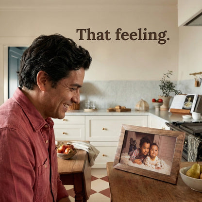 A 10-inch oak wood Family Frame WiFi photo frame bringing joy to a user standing in a warmly lit kitchen space. Crafted specifically as a heartwarming long-distance family gift, this smart picture frame instantly receives new photos from loved ones living far away. It functions as a powerful digital memory display to consistently spark joy and combat loneliness through shared daily experiences.
