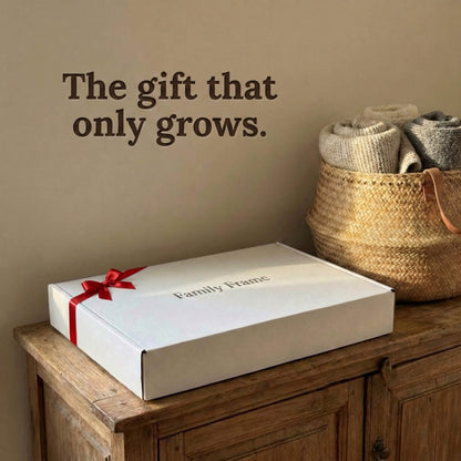 A 10-inch white Family Frame smart picture frame packaged securely in a premium branded white gift box with a red ribbon, resting on a rustic wooden console. Packaged specifically as a long-distance family gift, this WiFi photo frame is ready to deliver an out-of-the-box experience of pure connection. This top-tier electronic photo frame allows easy pre-loading of photos so families can start sharing memories the moment it is plugged in.
