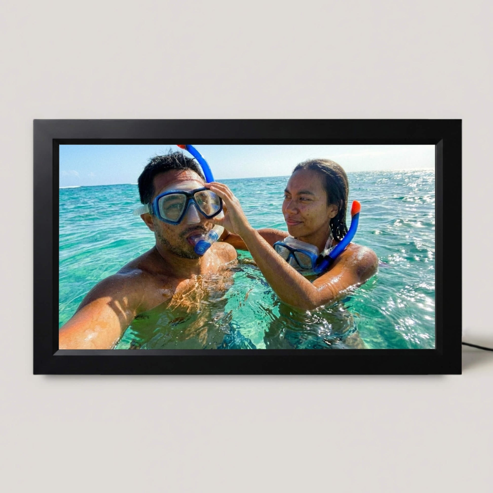 A 16-inch black Family Frame digital picture frame resting on a neutral surface, showcasing a vibrant edge-to-edge photograph without a mat. This sleek smart picture frame features a premium HD digital photo display designed to keep cherished memories central to everyday life. Functioning as the ultimate long-distance family gift, this WiFi photo frame seamlessly connects separated loved ones with absolutely zero subscription fees.
