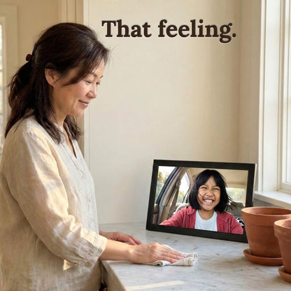 A 16-inch black Family Frame WiFi photo frame being viewed joyfully by a user wiping down her kitchen counter. Engineered specifically as a heartwarming long-distance family gift, this sleek smart picture frame instantly receives new photos from loved ones living far away. It functions as a powerful digital memory display to consistently spark joy and combat loneliness through effortless photo sharing.
