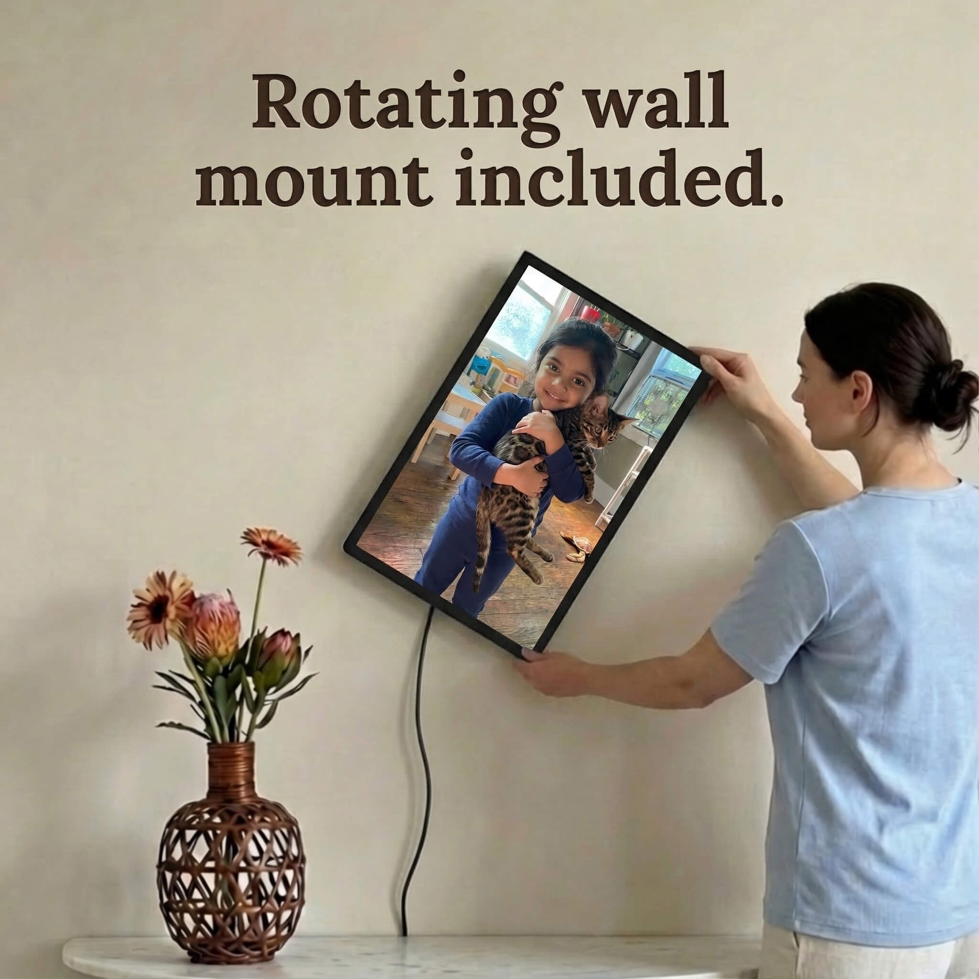 A 20-inch black Family Frame digital picture frame being rotated on a light-colored wall by a user to accommodate a vertical portrait photograph. This premium electronic photo frame includes an innovative rotating wall mount, allowing families to easily switch between landscape and portrait orientations without ever re-hanging the device. This high-end HD digital photo display reliably connects separated families with an elegant, wire-managed aesthetic.
