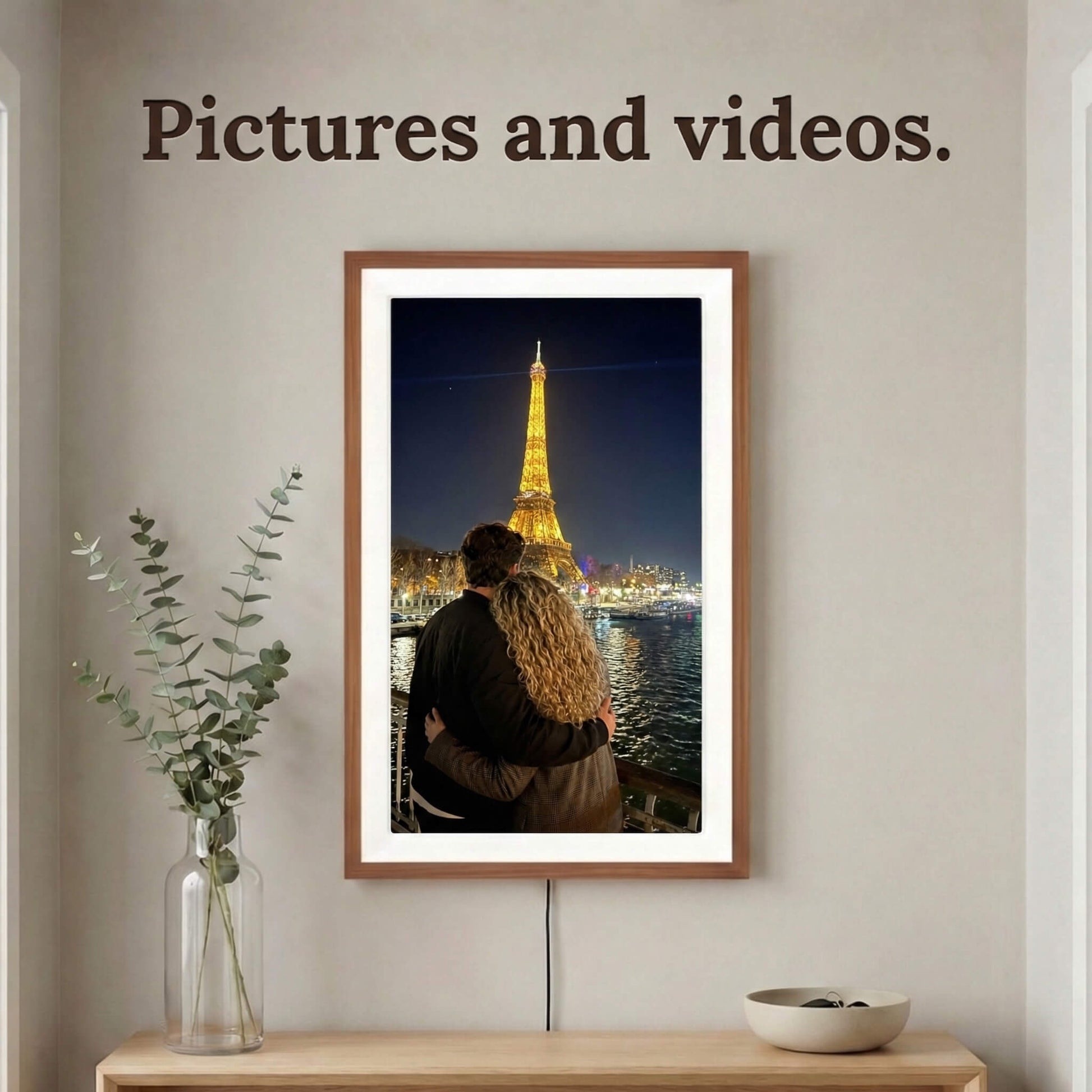 A vertically mounted 20-inch oak wood Family Frame digital memory display with an elegant white mat positioned above a light wood console table. Equipped with advanced processing, this premium digital picture frame flawlessly handles both high-definition photo and video playback to capture full, immersive memories. The robust photo sharing frame allows distant relatives to securely send video messages directly to the living room display.
