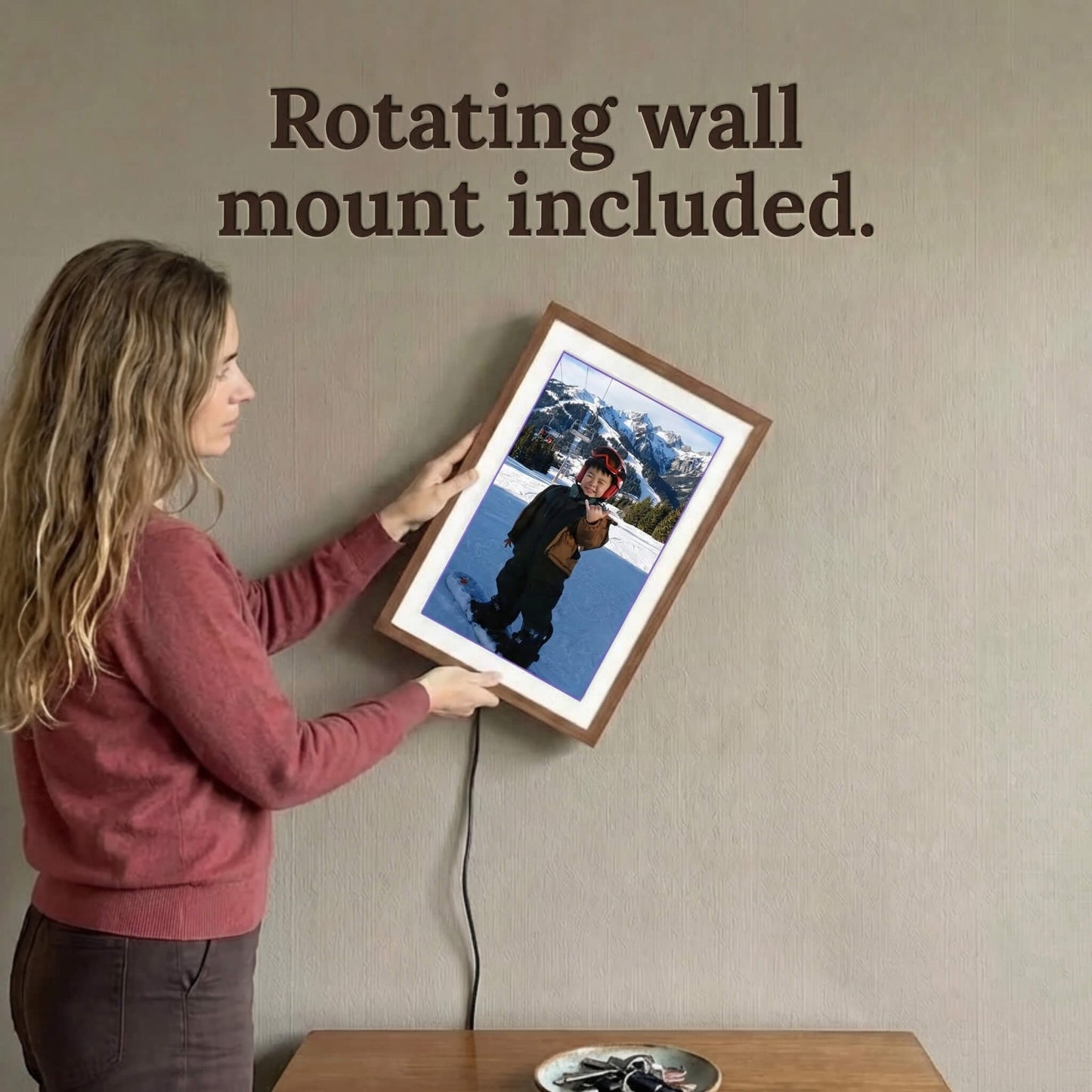 A 20-inch oak wood Family Frame digital picture frame being rotated on a textured wall by a user to accommodate a vertical portrait photograph. This premium electronic photo frame includes an innovative rotating wall mount, allowing families to easily switch between landscape and portrait orientations without ever re-hanging the device. This high-end HD digital photo display securely conceals its power cable while reliably connecting separated families.

