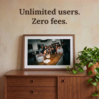 A 20-inch oak wood Family Frame digital picture frame with a clean white mat mounted prominently above a retro wooden credenza surrounded by lush plants. Built to gather the whole family, this expansive smart picture frame securely accepts photo uploads from an unlimited number of invited users around the globe. Operating entirely as a no subscription fee digital frame, it represents the most cost-effective way to maintain long-distance family connections over time.
